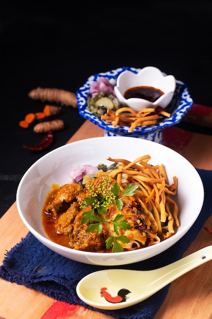 Thai Food concept Khao soi or Khao soy thai curry beef with egg noodles on wooden board on black background with copy space