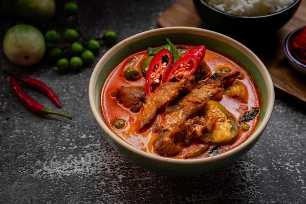 Thai food - spicy pork red curry with ingredients on dark table