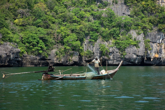 Thai man fisher people sailing wood long tail boat fishery floating in sea use net catch fishing marine and fish in ocean at Mu Ko Petra National Park at Pak Bara on April 12 2022 in Satun Thailand