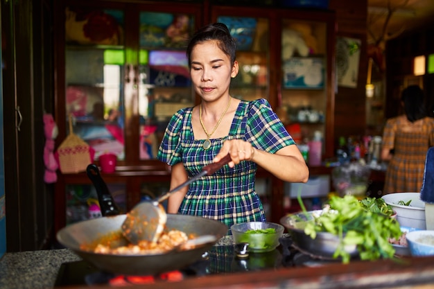 Thai mother cooking traditonal red curry in rustic home kitchen