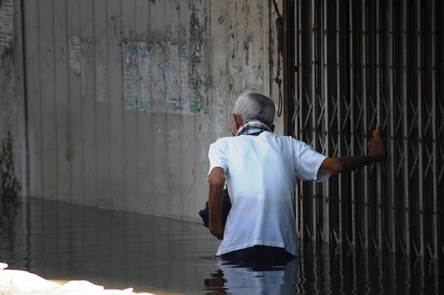 Thai old men people natural disaster victims walking wading in water on street while water flood and inundation road wait help rescue and donations at countryside rural city in Nonthaburi Thailand