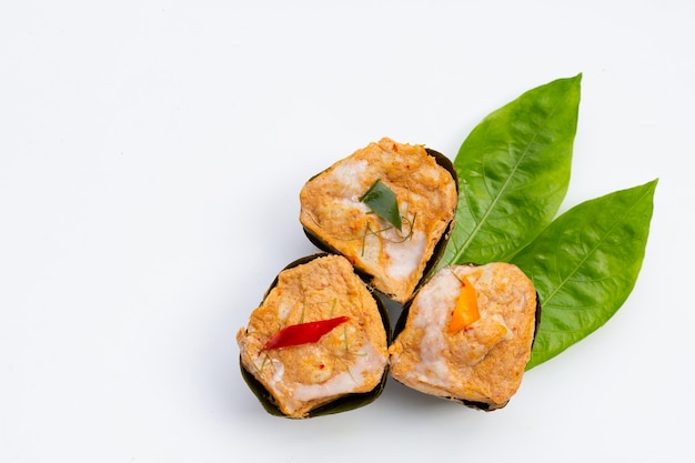 Thai streamed fish curry in banana leaves on noni or morinda citrifolia leaves on white surface