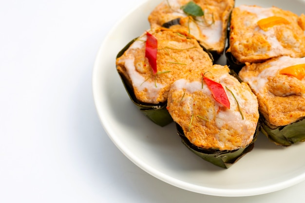 Thai streamed fish curry in banana leaves on white plate