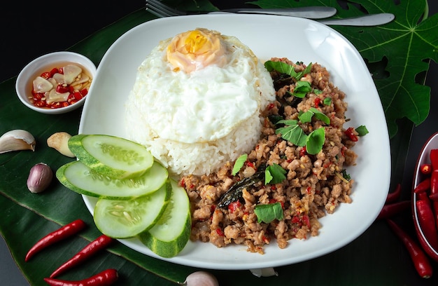 Thai street food basil fried rice minced pork fried egg and sliced cucumber on a black table