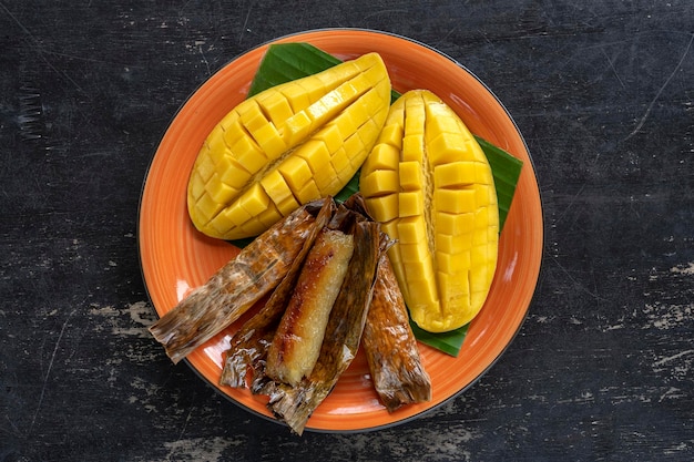 Thai style dessert yellow mango with banana sticky rice in palm leaves Yellow mango and sticky rice is popular traditional food of Thailand Closeup