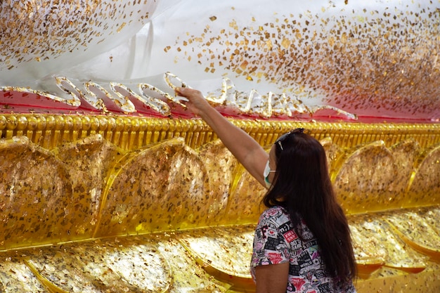 Thai travelers old women travel visit and cover thin gold leaf on buddha statue for respect praying blessing worship at Wat Buddha Saeng Tham Dharma practice office at Nong Khae in Saraburi Thailand