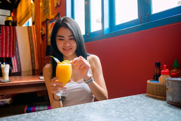 Thai woman drinking orange juice in a cafe Using laptop shopping online Work with a computer in a coffee shop