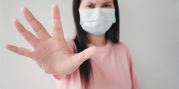 Thai woman wearing a face mask using a palm to show the stop of the coronavirus