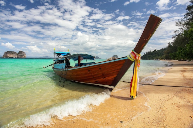 Thailand typical Long-tail boat on clear azure green sea, sky with small clouds above, golden beach on right, Koh Kradan island in Krabi region.