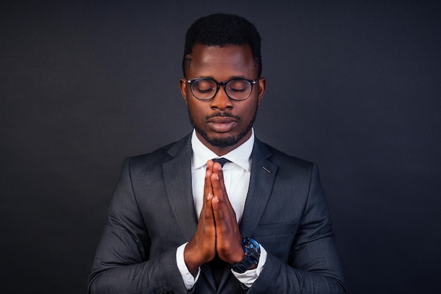 Thank God for all that I have. afro american business advisor man praying and meditating, hand sign calm gesture from the front black background in studio