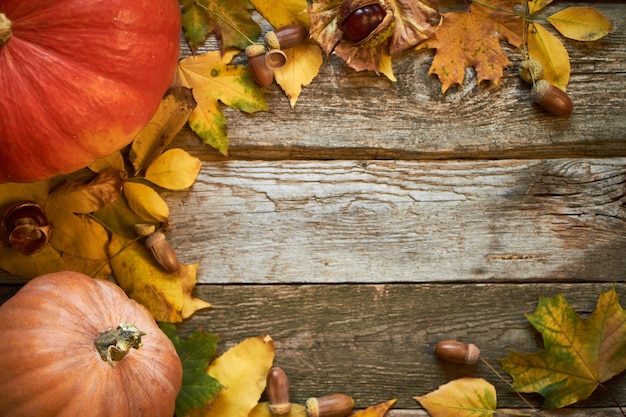 Thanksgiving autumn background on a dark wooden surface, pumpkins, withered leaves, acorns and chestnuts