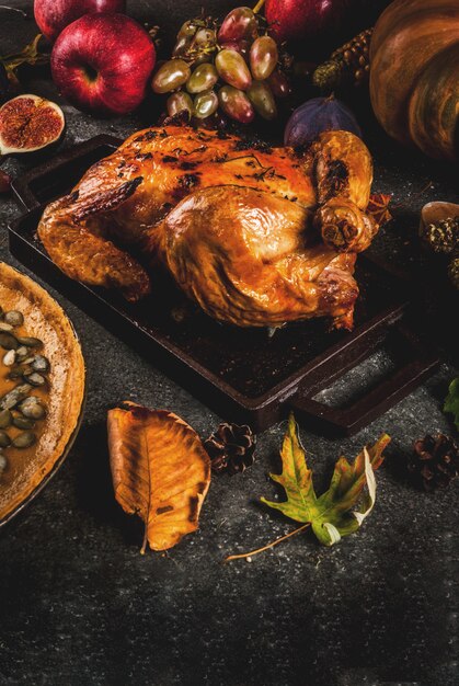 Thanksgiving Day food. Roasted whole chicken or turkey with autumn vegetables and fruits: corn, pumpkin, pumpkin pie, figs, apples, on dark grey , 