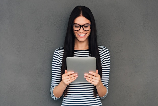 That is just great! Attractive young woman holding digital tablet and looking at it with smile standing