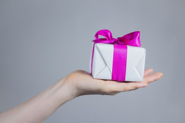 Theme of celebrations and gifts woman holding exclusive gift Packed in white box with purple ribbon beautiful and expensive gift on dark background