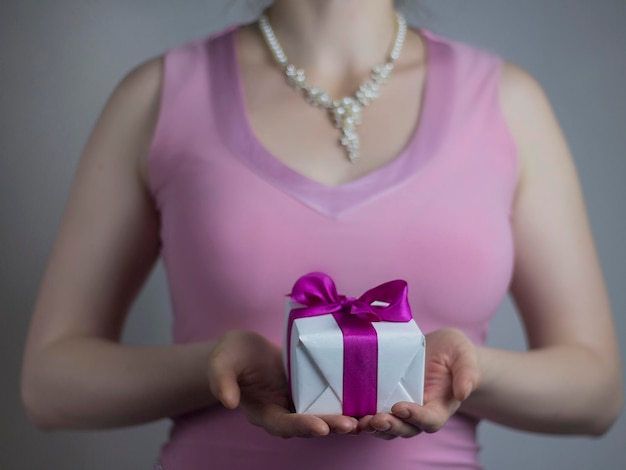 Theme of celebrations and gifts woman in pink dress holding a gift white box with purple ribbon