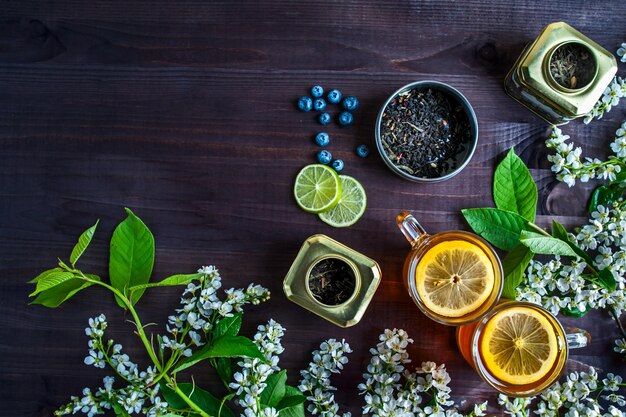 Theme of tea background with space for text dark Black tea in transparent mugs with lemon ginger lemons limes mint cherry blossoms Food industry tea packing restaurant business