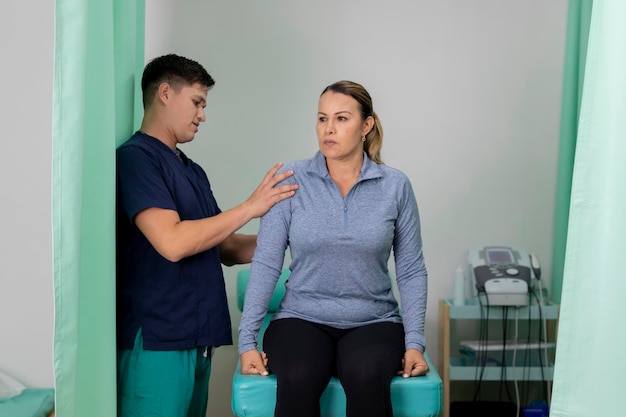 Therapist checks the shoulder of a woman who is sitting on the table in the office