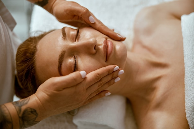 Therapist is doing face relaxing massage to a young woman in modern wellness cabinet