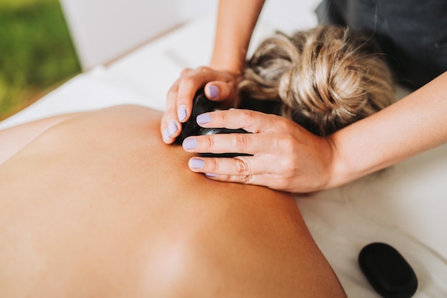 Therapist placing hot spa volcanic lava stone on a female patient's neck and back Energy stones