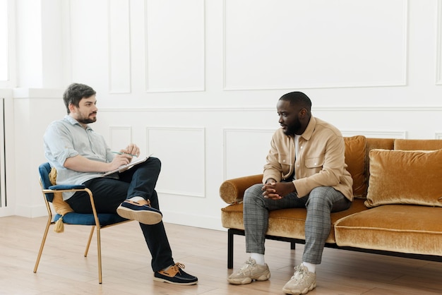 The therapist takes notes while talking to a depressed male patient and talks to an African man