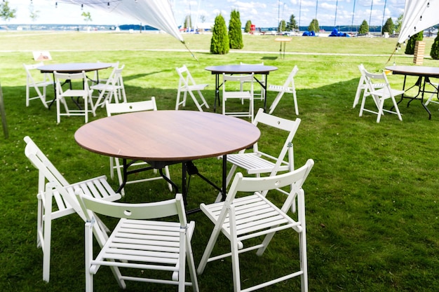 There are empty wooden tables and chairs on the green lawn Banquet service is preparing for the event Horizontal photo