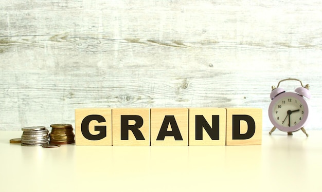 There are five wooden cubes with letters on the table next to the coins GRAND word On a gray background Front View Concepts