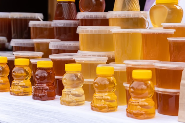 Photo there are many jars of organic natural honey on counter for sale different honey different colors in plastic cans are ready for sale at the honey fair nuts filled with honey