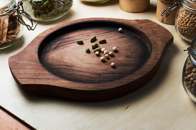 There are round wooden tray with few cardamom pods and pepercones and other indian spices around in glass jars.