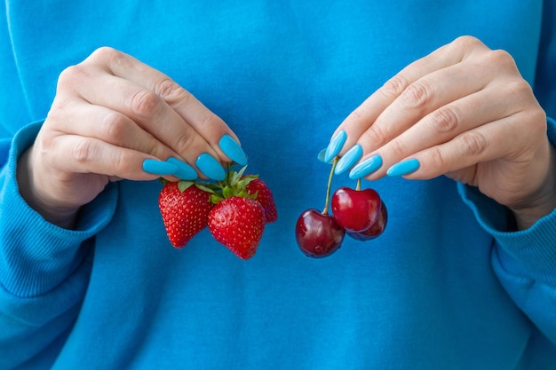 There are three strawberries in one hand and cherries in the other