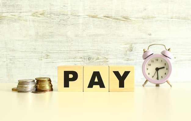 There are three wooden cubes with letters on the table next to the coins The word PAY On a gray background