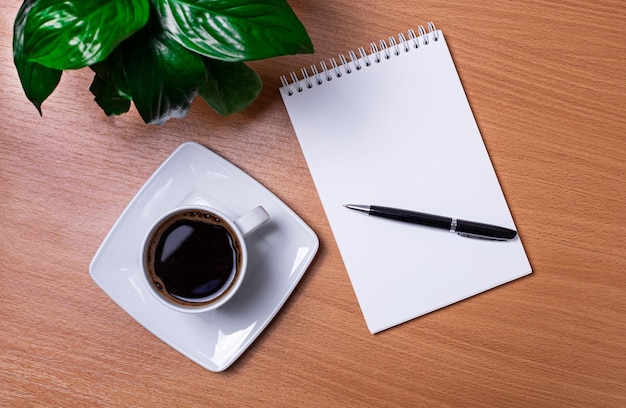 There is a green plant a white cup of coffee and an orange notepad with a pen on the desktop Business concept Closeup of the workplace Copy space