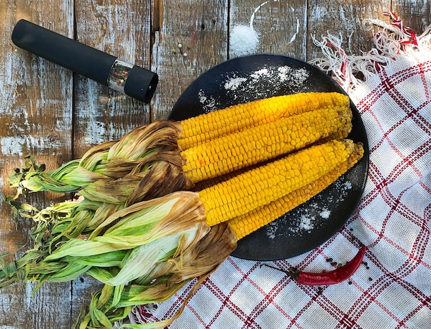 There is grilled corn on a black plate