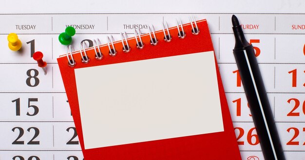 There is a red notepad and a black marker on the surface of the calendar. On a notepad, there is a blank white card with a place to insert text