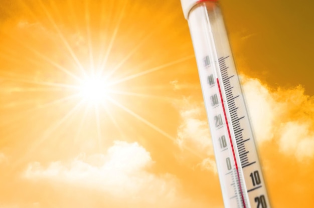 Thermometer against the background of an orange yellow hot glow of clouds and sun, concept of hot weather.