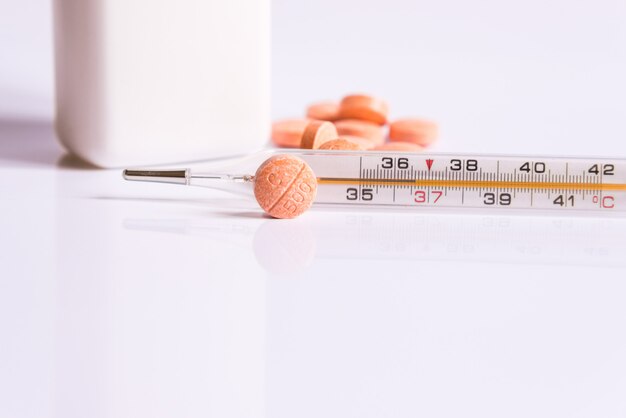 Thermometer and pills on a white background.