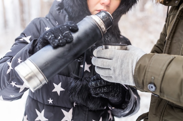 Thermos and cold season concept - A woman pours a hot drink. Couple on a winter holiday.