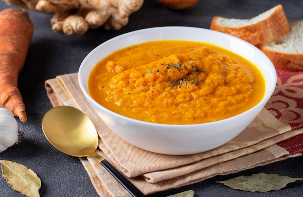 Thick carrot cream soup with ginger and garlic in a white bowl on a dark background