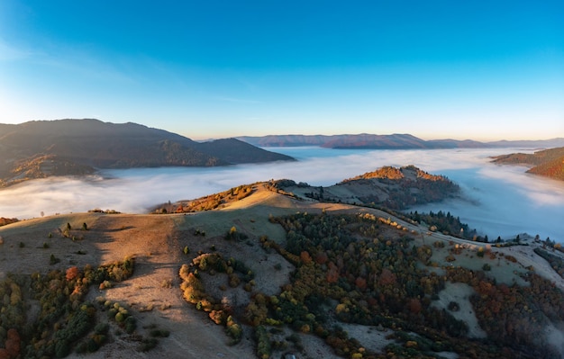 Thick fog among peaks of high autumn mountains at sunrise