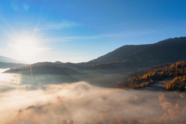 Thick layer of fog covering high mountains with terracotta and green trees growing under bright blue cloudless sky panorama view