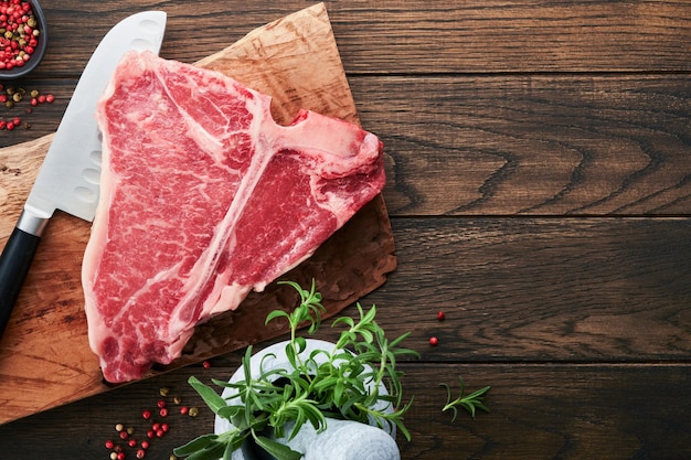 Thick Raw TBone Steak Dryaged Raw Tbone or porterhouse beef meat Steak on cutting boar with herbs and salt on dark background Top view and copy space