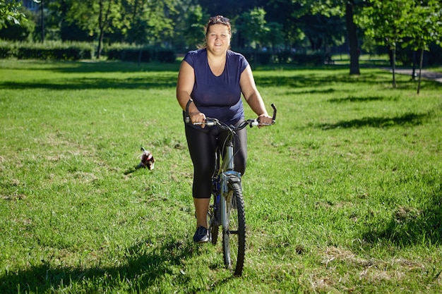 Thick white woman cycling in public park of sunny summer day