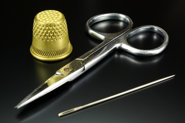 Thimble scissors and needle on black