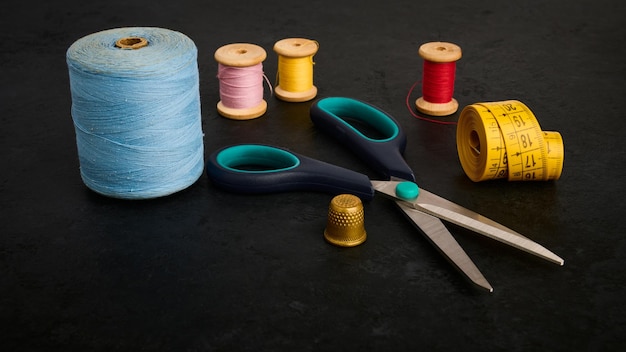 Thimble scissors tailor's meter and bobbin with thread on black table shallow depth of field