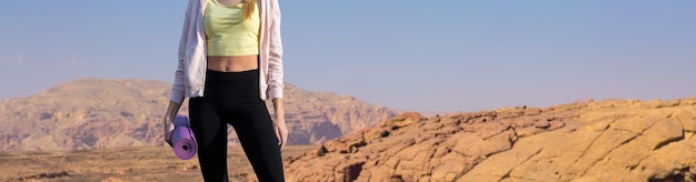 A thin athletic girl takes a break between classes on the background of mountains in the early morning