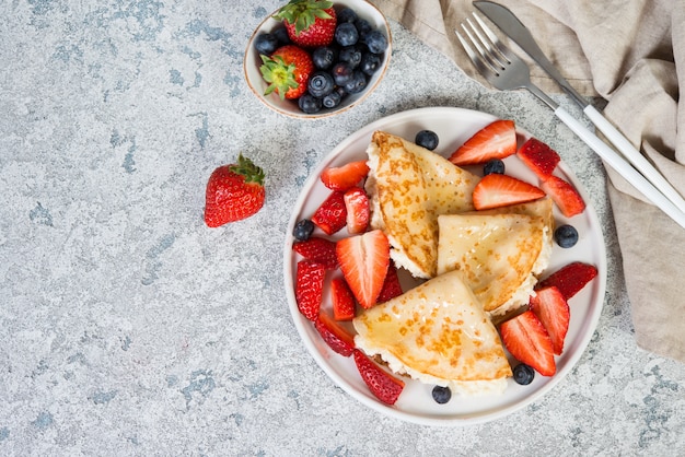 Thin crepes with ricotta cheese and fresh strawberries on a gray concrete background.