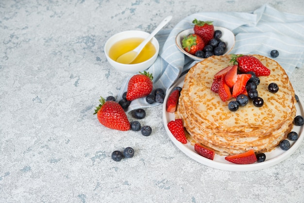 Thin homemade pancakes in a plate with fresh berries and honey, copy space