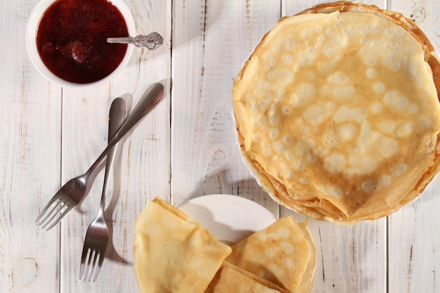 Thin hot pancakes with strawberry jam on a white wooden table Holiday Maslenitsa