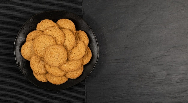 Thin oatmeal cookies mockup. Healthy cereal oat crackers top view on black background. Crispy anzac biscuit cookie with oat flakes with copy space