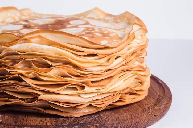 Thin pancakes on a round wooden stand on a white surface