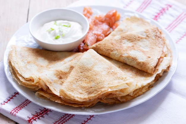 Thin pancakes with salmon and sour cream on a light background rustic style